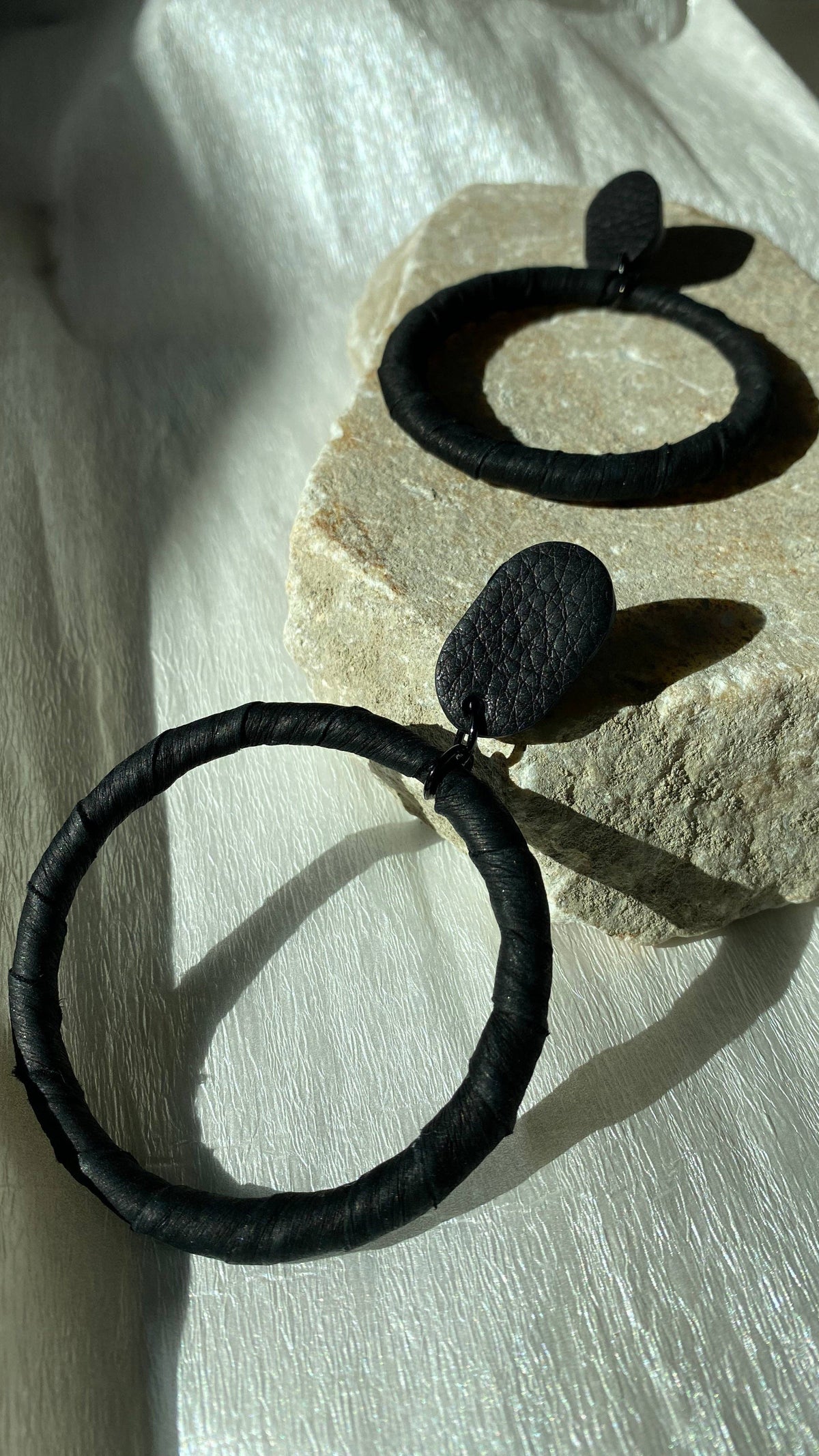 Black hoop earrings with leaf accents on a stone surface