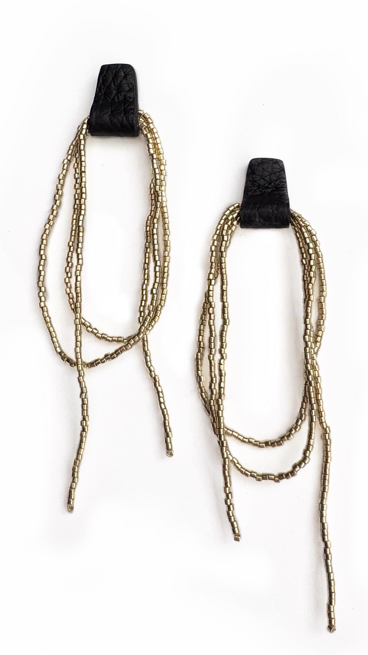 A pair of statement dangle earrings featuring textured black top caps and multiple strands of metallic gold thread hanging below, set against a plain white background.